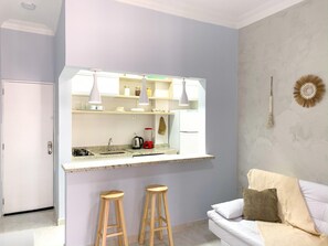 A compact living space with a kitchenette, a white sofa, and two wooden stools. - 6 Minutes From Copacabana Beach Br1033 (Rio de Janeiro)