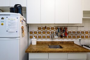 Cucina con mobili bianchi, piano di lavoro in granito, lavello e schienale decorato con un motivo floreale.