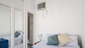 Habitación de hotel con cama, espejo, aire acondicionado instalado en la pared y una puerta que da a otra habitación.