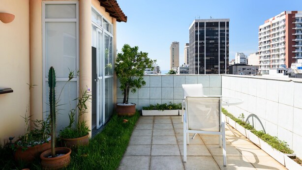 Un patio en la azotea con una silla blanca, plantas en macetas y vistas de edificios altos.