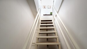 A staircase with white railings and wooden steps leading to a landing with two framed pictures and a plant.