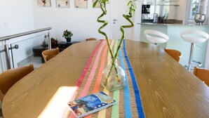 A wooden dining table with a colorful striped placemat, a glass vase with a plant, and a magazine.