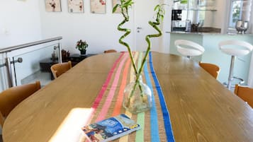 Una mesa de comedor de madera con un posavasos a rayas de colores, un florero de vidrio con una planta y una revista.