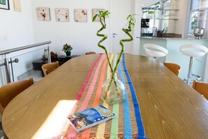Ein Holztisch mit einer farbenfrohen Streifen-Platzset, einer Glasvase mit Pflanze und einer Zeitschrift.