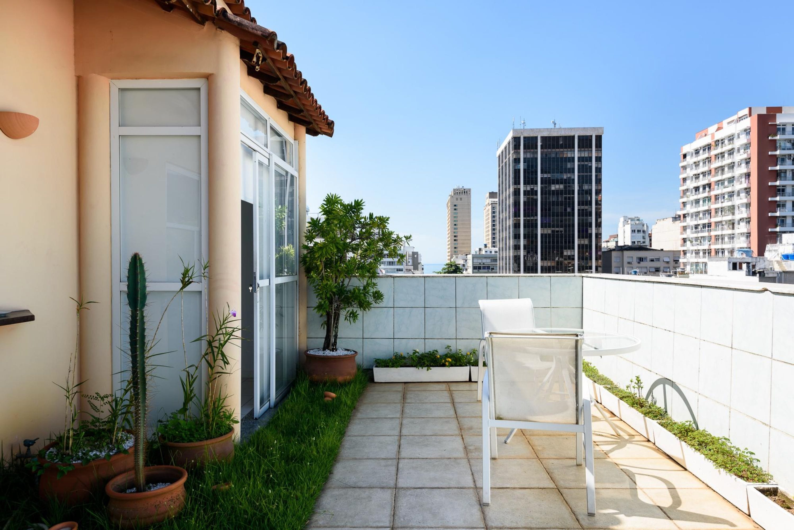 Une terrasse sur le toit avec une chaise blanche, des plantes en pot et une vue sur de hauts immeubles.
