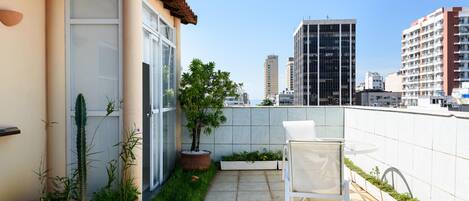 Une terrasse sur le toit avec une chaise blanche, des plantes en pot et une vue sur de hauts immeubles.