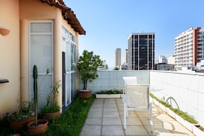 A rooftop patio with a white chair, potted plants, and a view of tall buildings. - Penthouse in Ipanema Christ View Mqc502 (Rio de Janeiro)