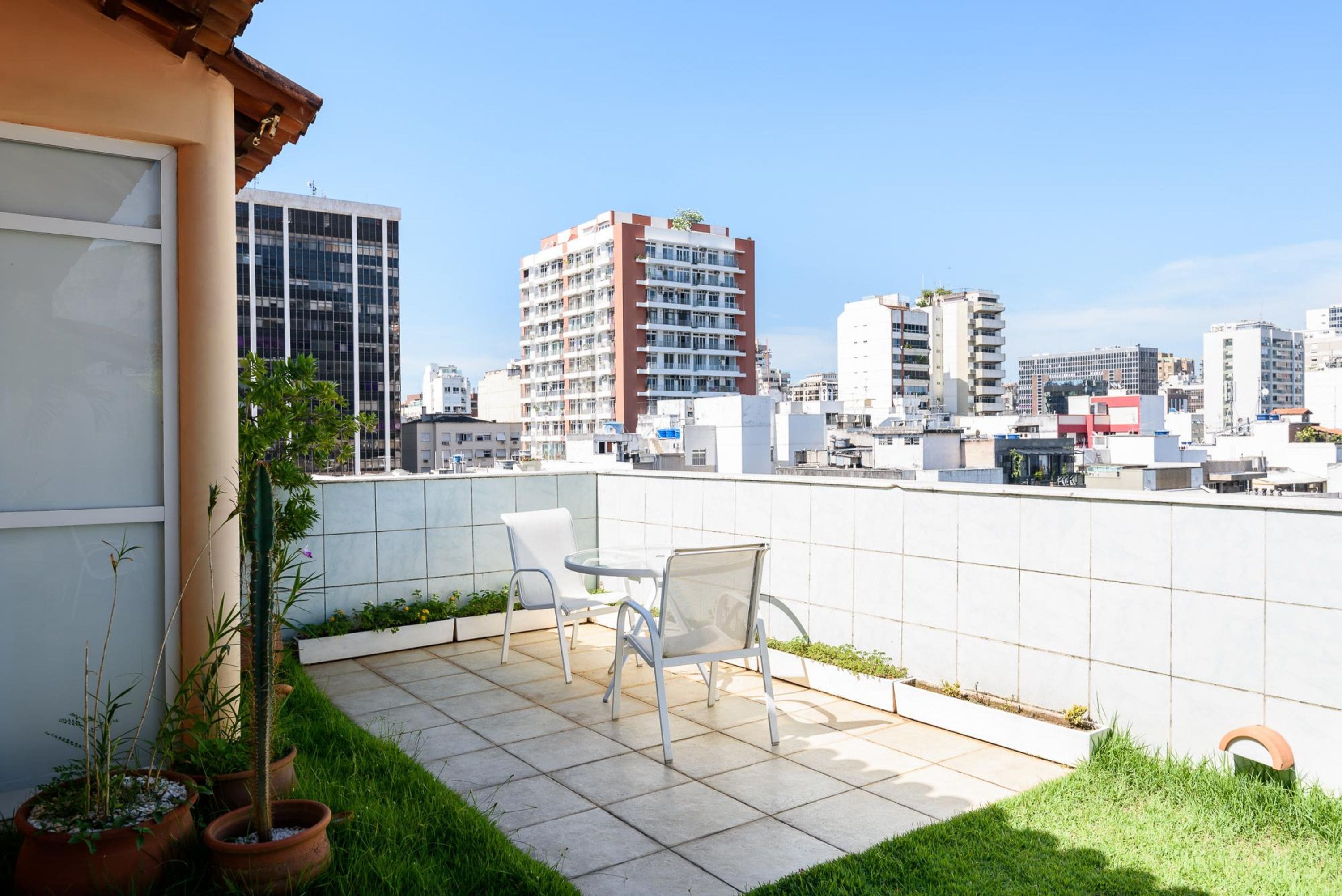 Eine Dachterrasse mit Tisch und Stühlen, Blumentöpfen und Blick auf die Stadt.