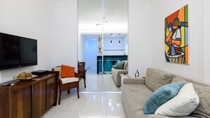 A modern living room with a flat-screen TV, a wooden console table, a sofa with patterned cushions, and a colorful abstract painting on the wall.