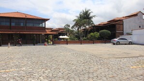 Um pátio com pavimento de pedras irregulares, um carro estacionado e edifícios com telhados de telha vermelha.