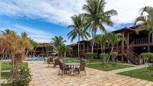 Pátio de hotel com piscina, palmeiras e área de estar com cadeiras e mesas.