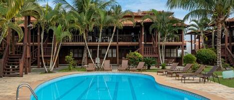 A swimming pool surrounded by palm trees and a building with a tiled roof.