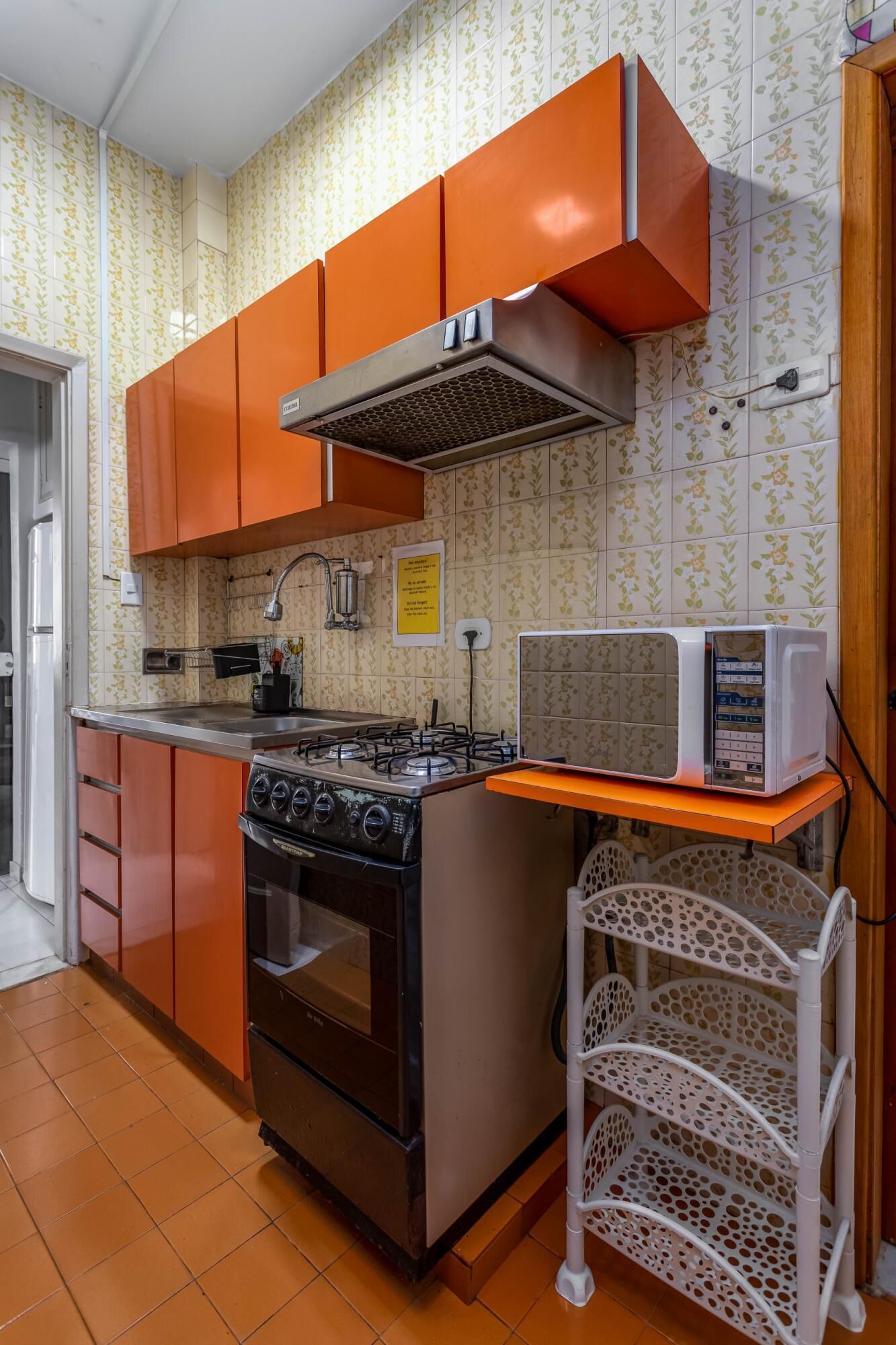 A kitchen with orange cabinets, a gas stove, a microwave, and a sink.