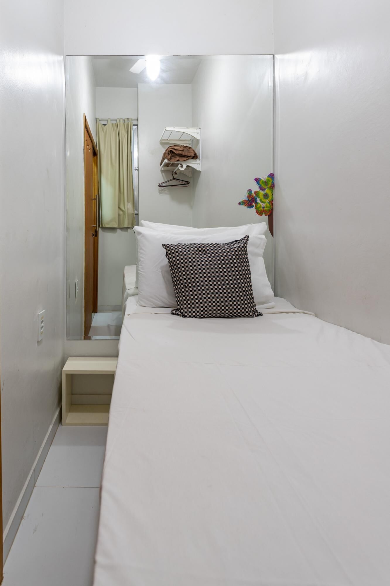 A small, neatly arranged bedroom with a bed, a hanging towel, and a butterfly decal on the wall.