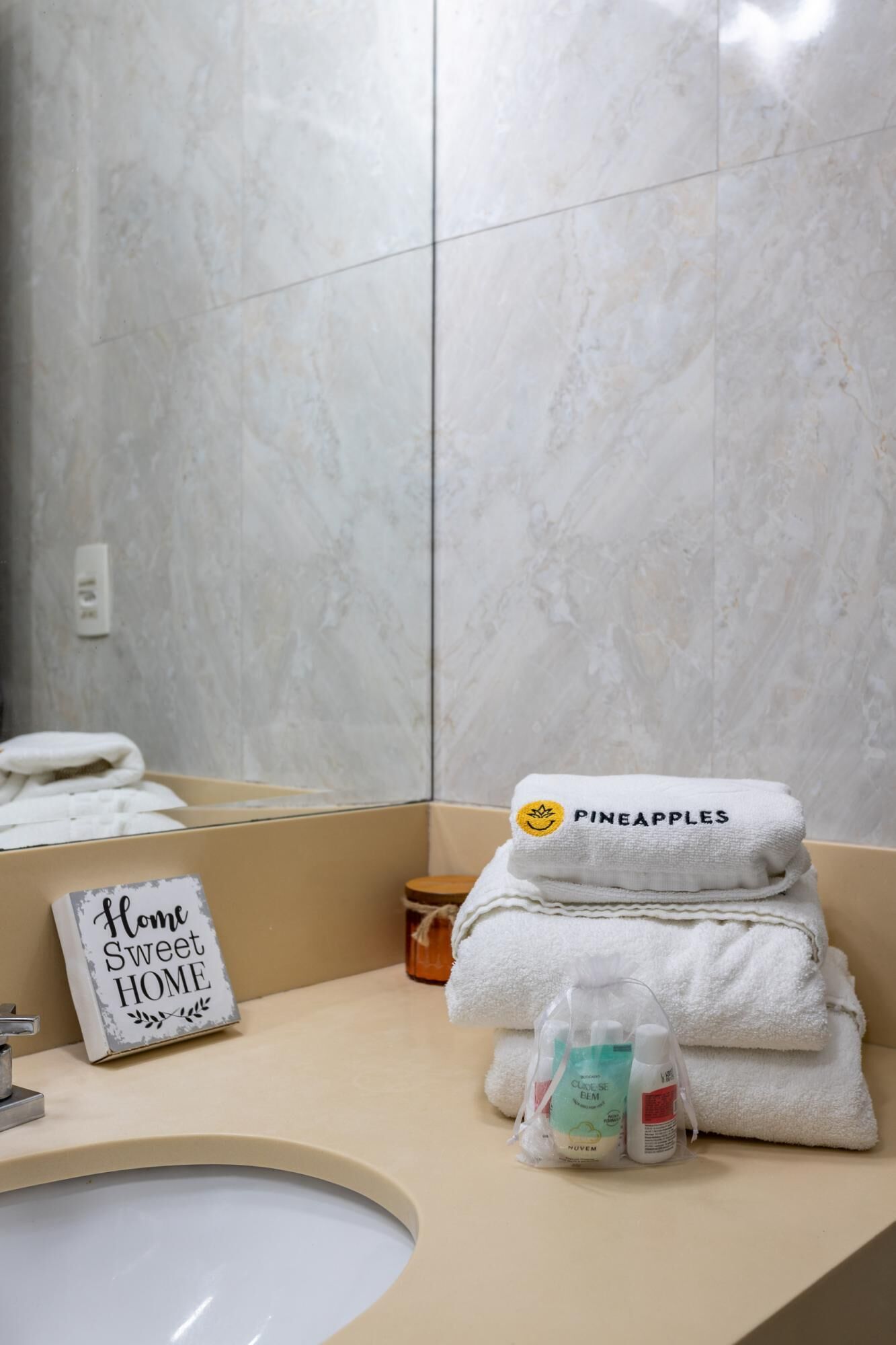 A bathroom with a marble wall, a sink, a towel rack with folded towels, a small bottle, and a sign that reads "Home Sweet Home".