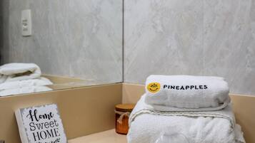 Un baño con pared de mármol, un lavamanos, un perchero con toallas dobladas, una pequeña botella y un cartel que dice 'Home Sweet Home'.