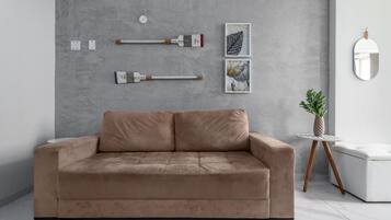 A modern living room with a beige sofa, a small round table with a potted plant, and wall-mounted art pieces.