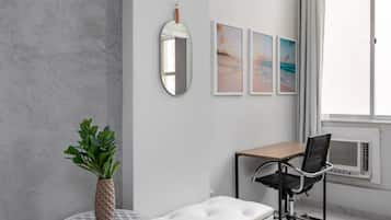 A modern living room with a white sofa, a round table with a plant, and a black office chair.