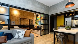 A modern living room with a grey sofa, a dining table, and a kitchen area with a fridge and stove. - 5 Minutes From Copacabana Beach Nsc902 (Rio de Janeiro)