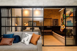 A modern hotel room with a grey sofa, a bed, and a small desk area.