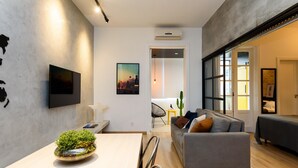 A modern living room with a grey sofa, a dining table with a plant centerpiece, and a flat-screen TV mounted on the wall. - 5 Minutes From Copacabana Beach Nsc902 (Rio de Janeiro)