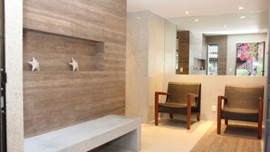 Een moderne lobby met een stenen bank, twee rieten stoelen en een wandplank met decoratieve sterren.
