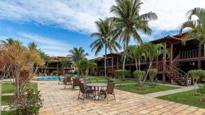 Een resort met een zwembad, terras, palmbomen en een twee verdiepingen tellend gebouw met een houten gevel.