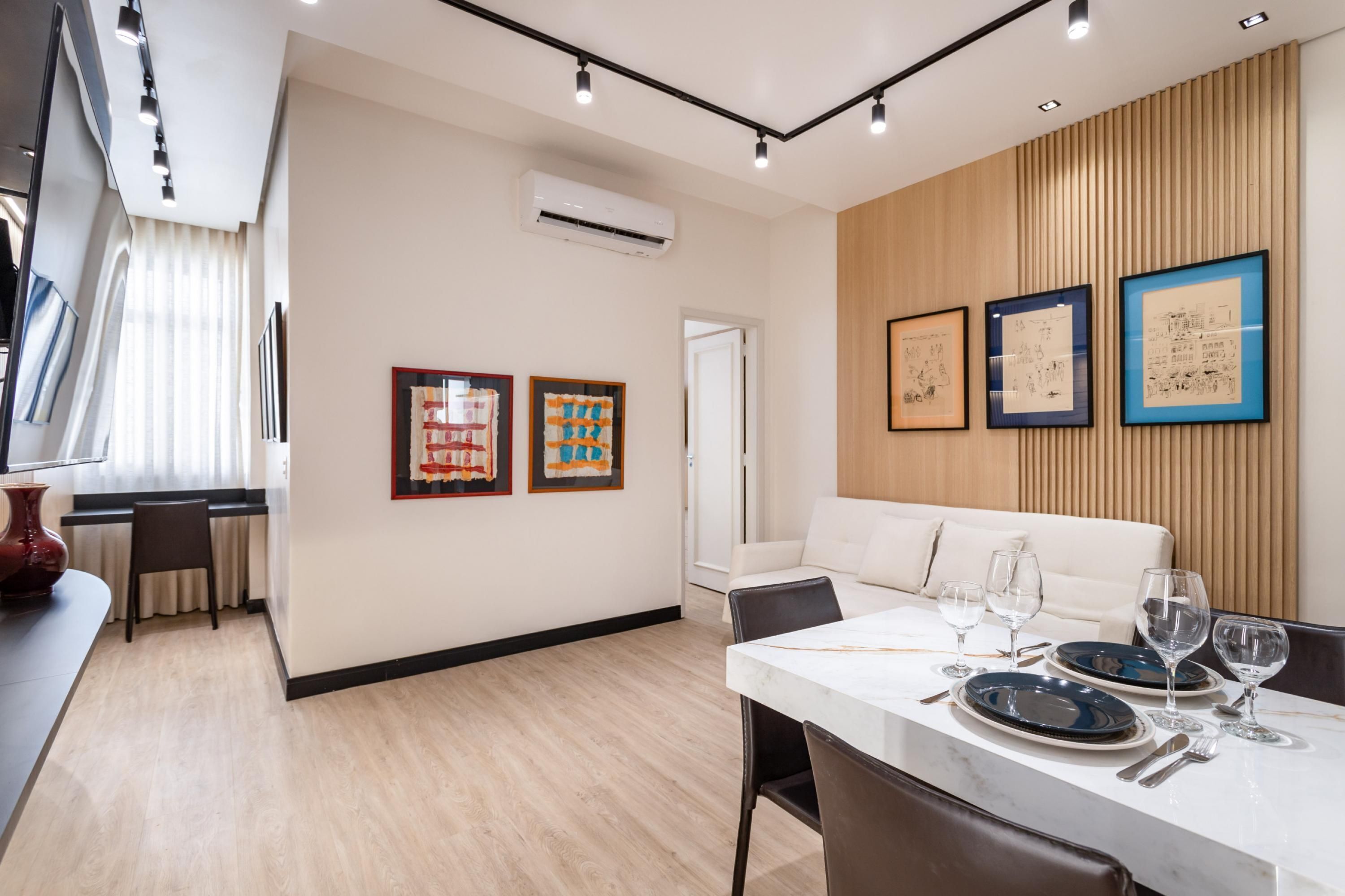 Un comedor moderno con una mesa de mármol, sillas y un sofá blanco. Hay obras de arte enmarcadas en la pared y un equipo de aire acondicionado sobre el sofá.