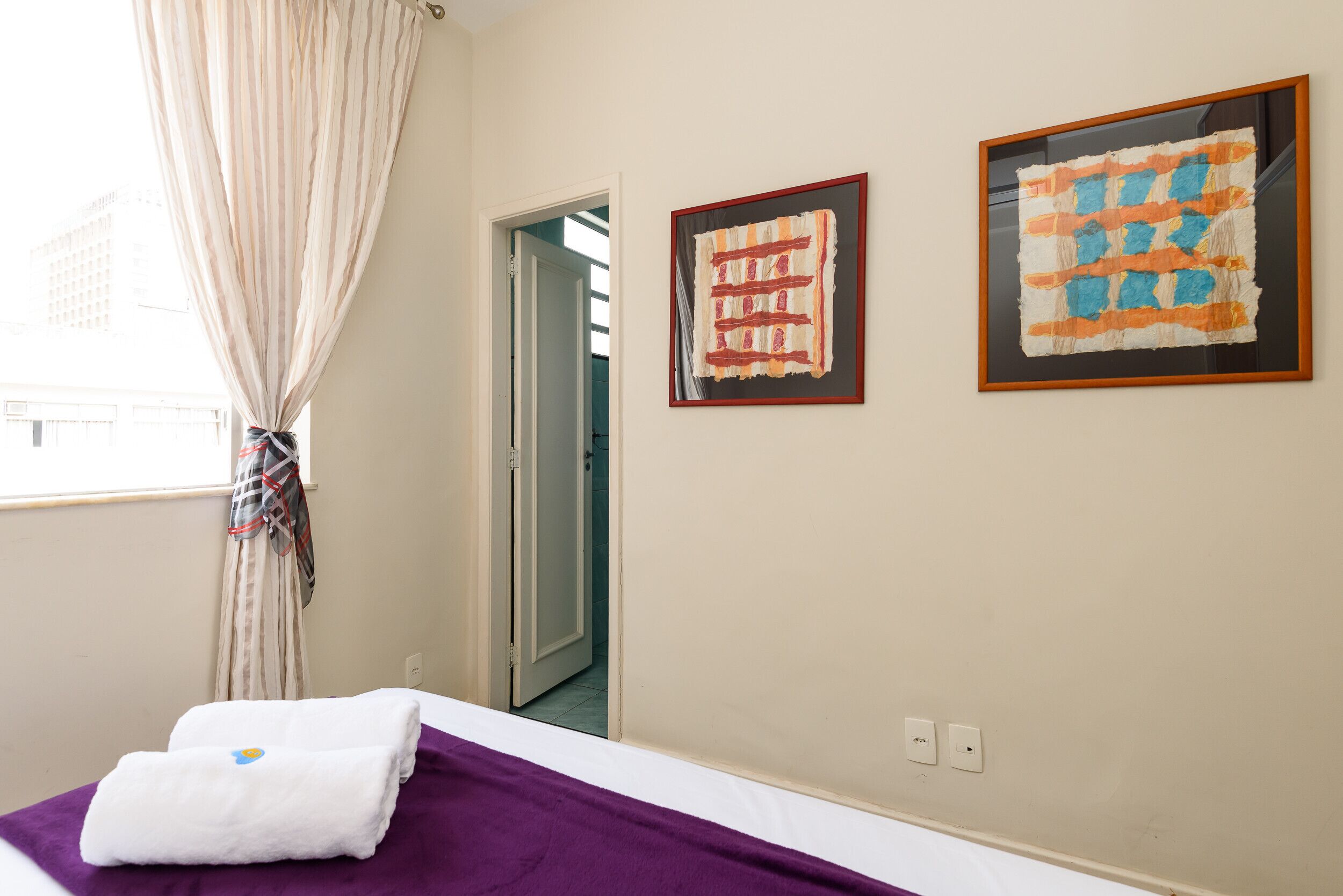 Una habitación de hotel con una cama, una manta púrpura, una toalla blanca y dos cuadros en la pared.
