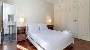 Un dormitorio con cama, mesitas de noche, armario y baño con lavamanos y espejo.