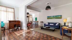 Amplia sala de estar con una mesa de centro de madera, un sofá azul y un comedor con un escritorio y sillas de madera.