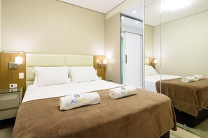 Ett hotellrum med en säng, två sidobord, en spegel och handdukar med logotypen ”ALL in RIO”.