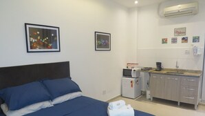 Quarto com cama, pequeno espaço de cozinha e ar-condicionado fixado na parede.