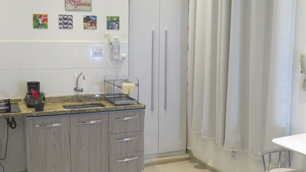 Uma cozinha com bancada de granito, cafeteira, pia e armário com gavetas. Inclui decorações nas paredes, como um letreiro de boas-vindas e uma foto do Rio de Janeiro.