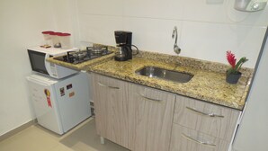 Uma cozinha compacta com fogão a gás, cafeteira, micro-ondas e pia.