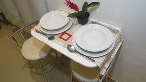 Uma pequena mesa de jantar com duas travessas brancas, uma colher e um vaso com planta.