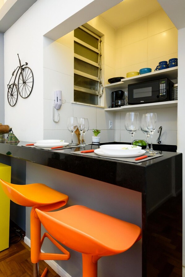 A modern kitchen with a black countertop, white tiles, a bicycle decoration, and orange bar stools. - Peace in Copacabana Forest View Br1009 (Rio de Janeiro)