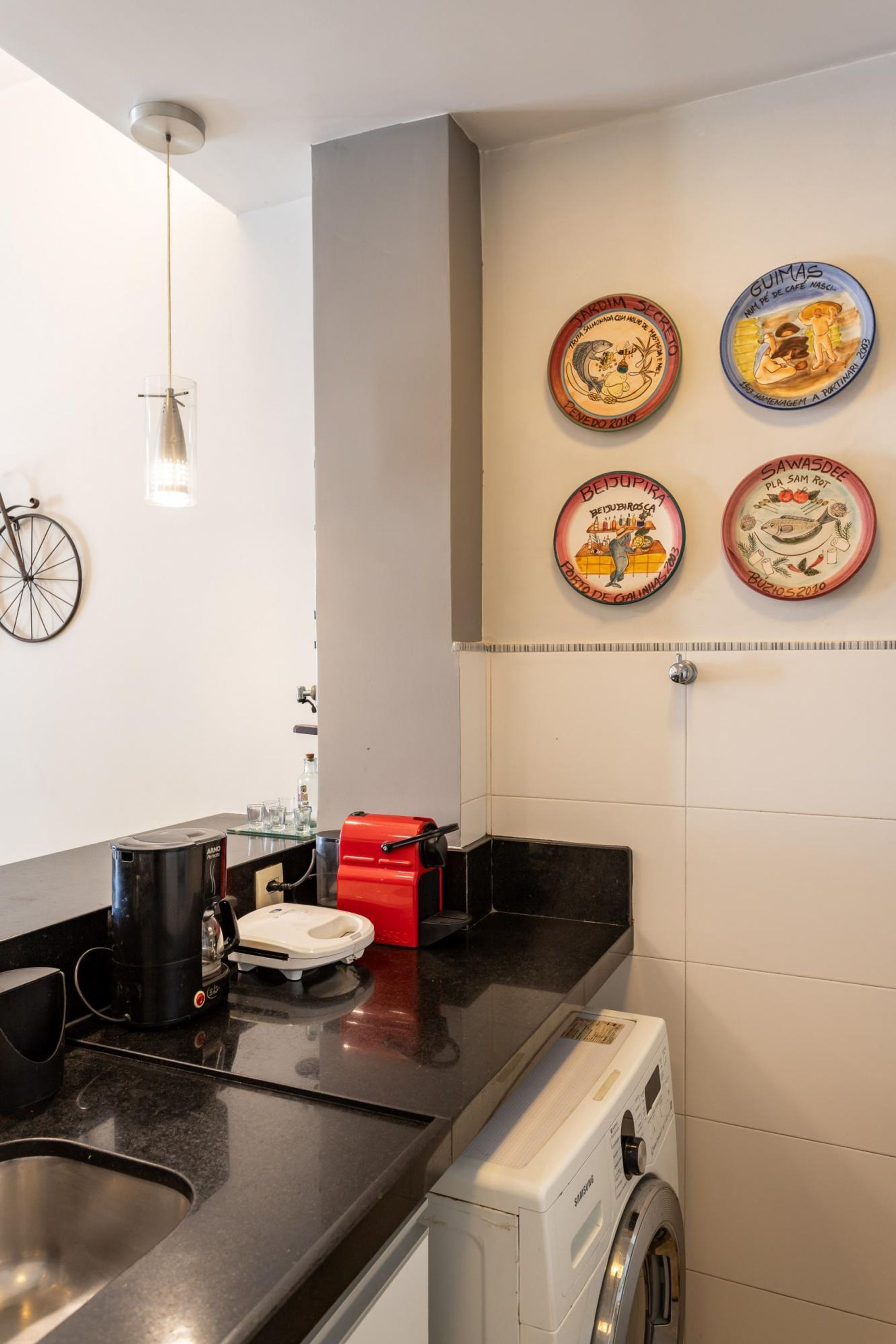 Eine Küche mit Kaffeemaschine, Toaster und Waschmaschine. An der Wand befinden sich Teller, und ein Fahrrad hängt dort.