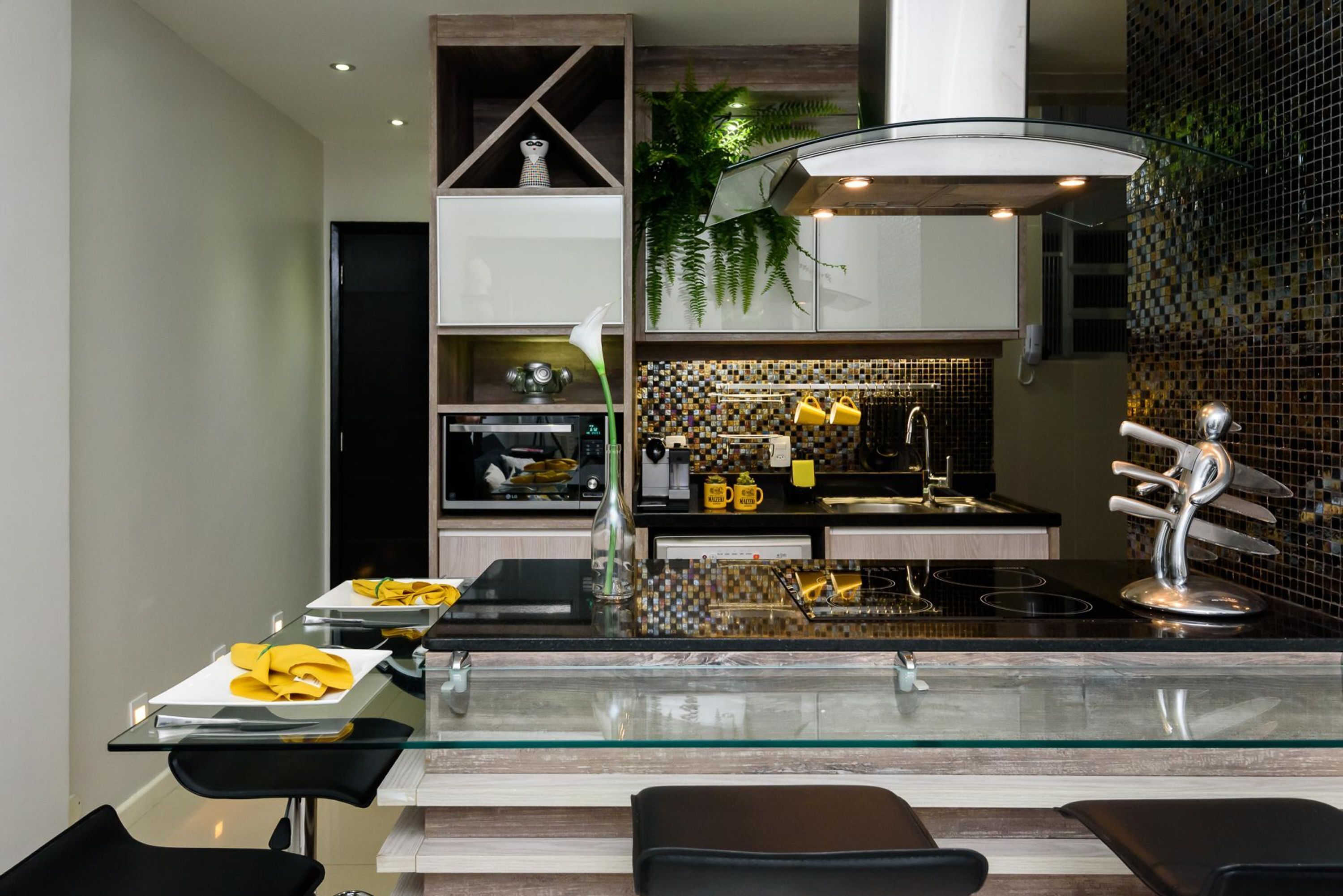 Une cuisine moderne avec un plan de travail en verre, des tabourets de bar noirs et une sculpture métallique décorative.