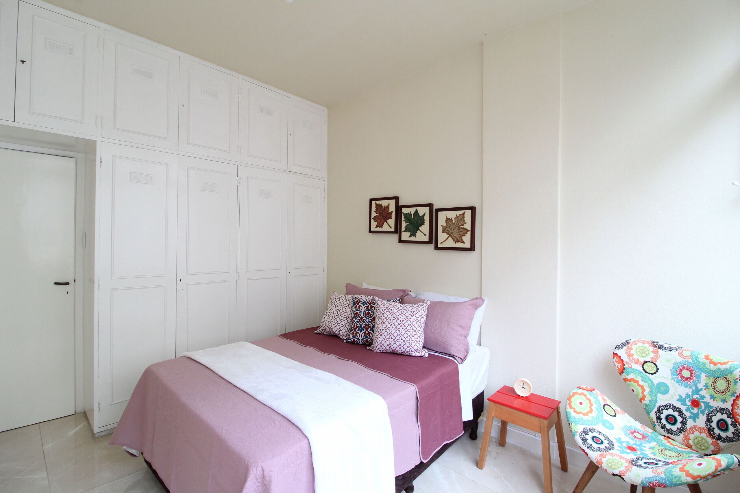 A bedroom with a bed, a chair, a small table, and a wardrobe.