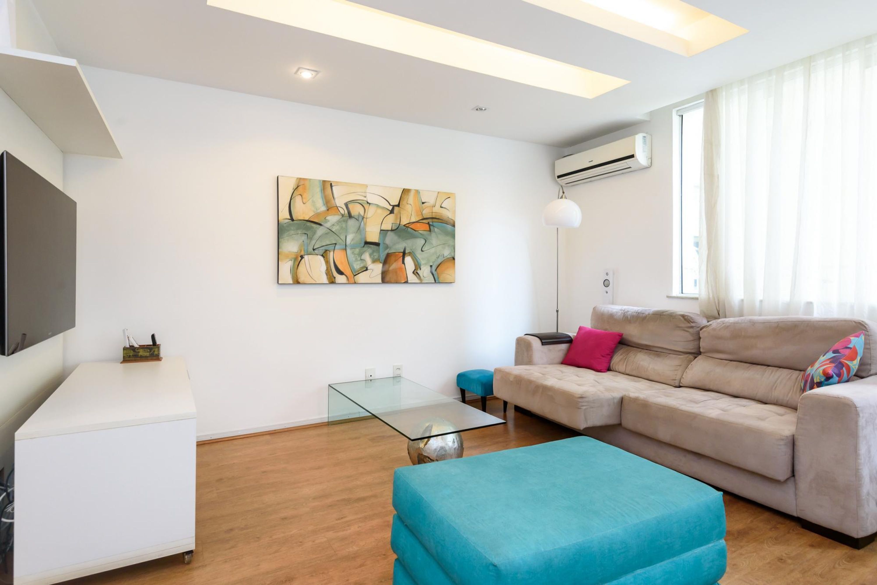A modern living room with a sofa, ottoman, glass coffee table, and artwork on the wall.