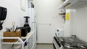 Uma cozinha compacta com fogão a gás, micro-ondas, torradeira e liquidificador em uma prateleira.