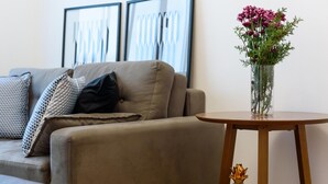 Uma sala de estar com um sofá, uma pequena mesa de madeira e um vaso com flores.