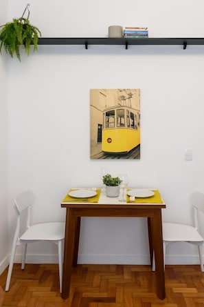 A dining area with a table set for two, a potted plant, and a wall-mounted picture of a tram. - 6 Minutes From Ipanema Beach Gc707 (Rio de Janeiro)