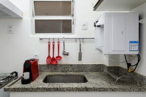A kitchen with granite countertops, a stainless steel sink, a red coffee maker, and various utensils hanging on a rack. - 6 Minutes From Ipanema Beach Gc707 (Rio de Janeiro)