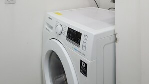 A compact, white washing machine with a digital control panel, a power outlet, and a wall-mounted heater above it. - 6 Minutes From Ipanema Beach Gc707 (Rio de Janeiro)