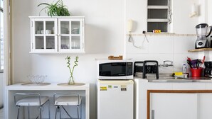 Cozinha compacta com micro-ondas, torradeira e um pequeno frigorífico. Há dois bancos altos e um armário sobre o balcão.
