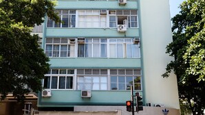 Um edifício com vários andares, fachada verde, várias unidades de ar condicionado e um grande outdoor publicando sapatos.