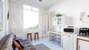 Espaço compacto com sofá, pequena cozinha incluindo micro-ondas e mesa de jantar.