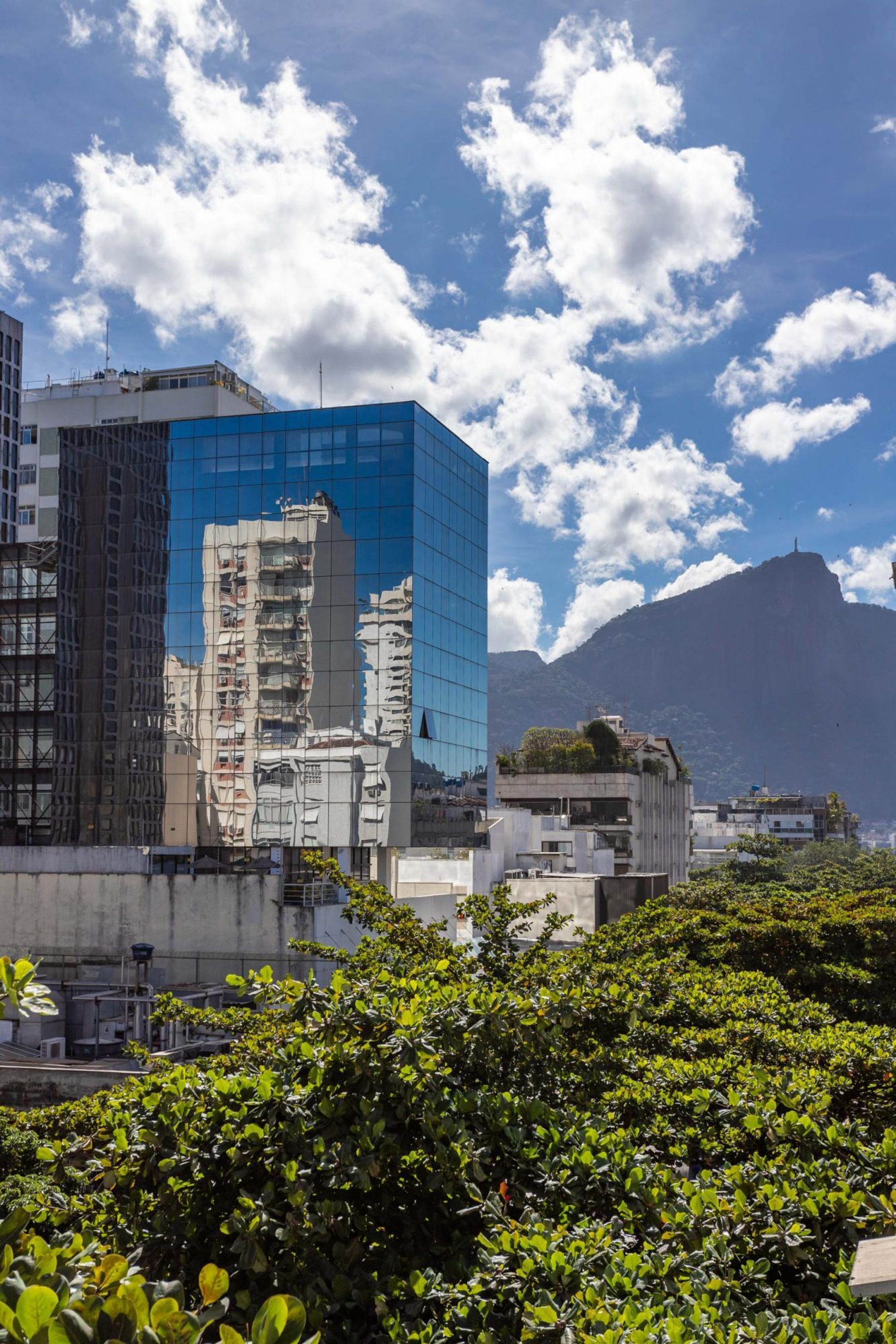 A modern building with a glass facade, surrounded by lush greenery and a mountainous backdrop.